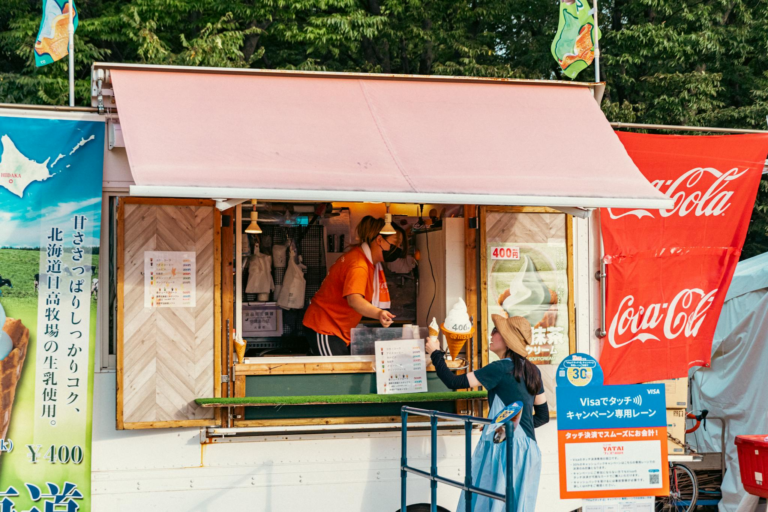 A vibrant street food stall in Japan with a customer buying ice cream during the day.